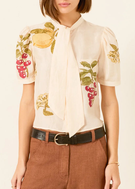 a cream-colored short-sleeve blouse by Alix of Bohemia with a tie-neck detail and colorful embroidered fruit motifs